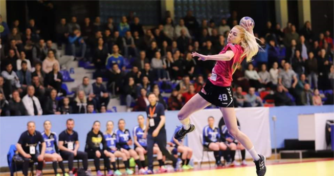 Në foto shihet një hendbolliste e cila është hedhur lartë me top në dorë për të shënuar gol.