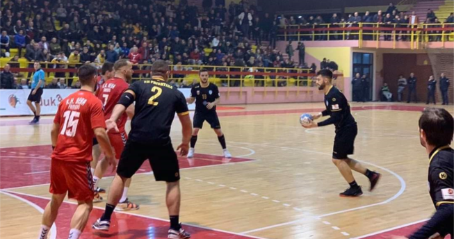 Lojtari ka topin në dorë dhe po vrapon, dy bashkëlojtarë të tij po i ndihmojnë duke u munduar t’i ndalojnë dy lojtarët kundërshtarë që mos t’a pengojnë gjuajtjen e lojtarit që ka topin.