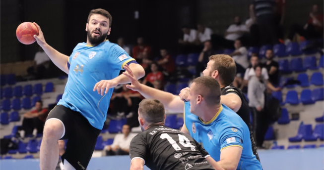 Një lojtar ka topin në dorë dhe është hedhur lartë për të shënuar, një bashkëlojtar i tij është aty që t'a ndihmojë, kurse dy kundërshtarë mundohen të e ndalojnë.