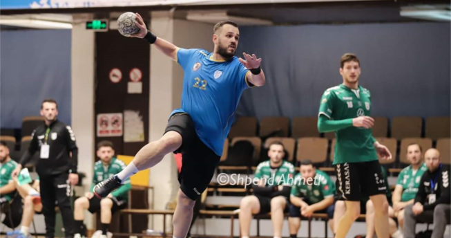 Lojtari ka topin në dorë dhe po tenton t’a gjuajë në portë, mbrapa tij është një lojtar kundërshtar.