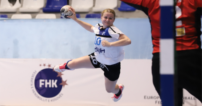 Një lojtare me top në dorë po mundohet të shënojë gol, kurse portierja kundërshtare tenton t'a ndalojë golin.